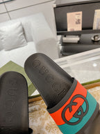 Black Gucci slide sandal with embossed upper and orange/teal logo strap