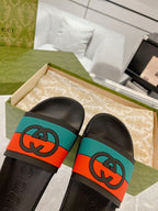 Black Gucci slide sandals with embossed logo insoles and orange/teal logo straps