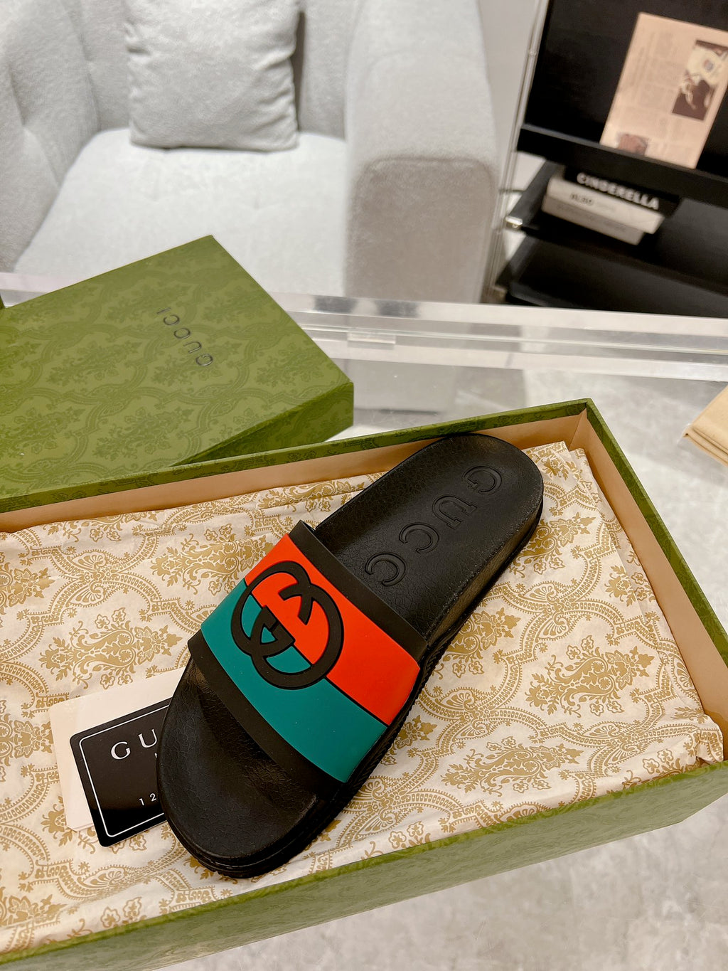 Black Gucci slide sandal resting in box; embossed logo footbed with orange/teal band