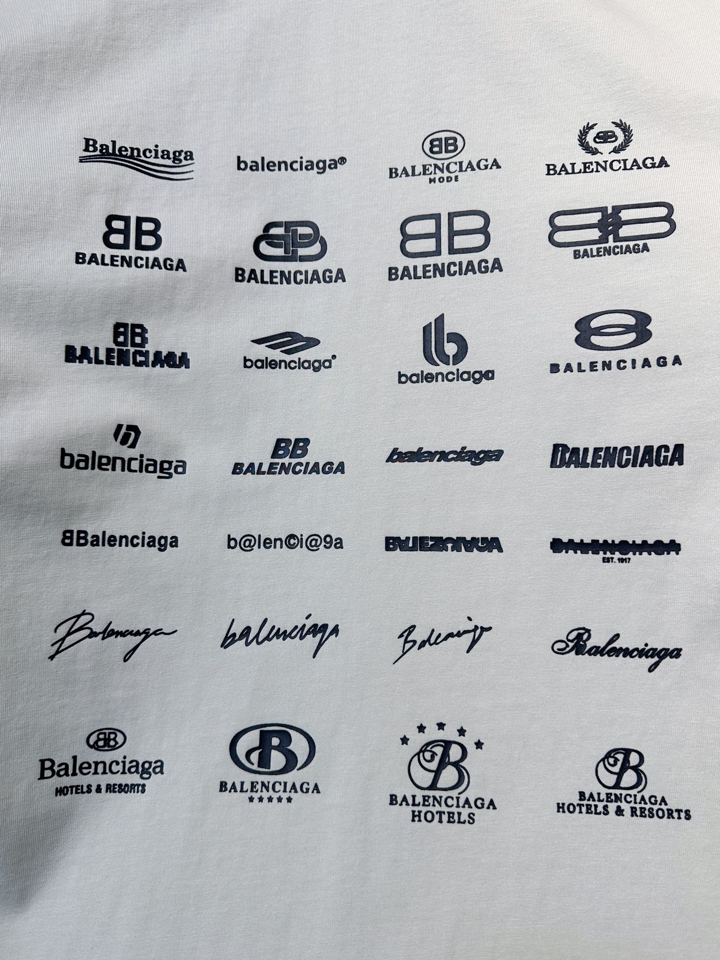 White T-shirt fabric with repeating black logo prints and signature-style marks