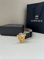 Black leather belt with croc texture and gold Medusa buckle on display.