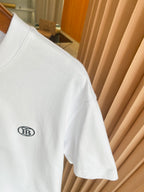 White T-shirt sleeve and side seam with small black chest logo patch detail.
