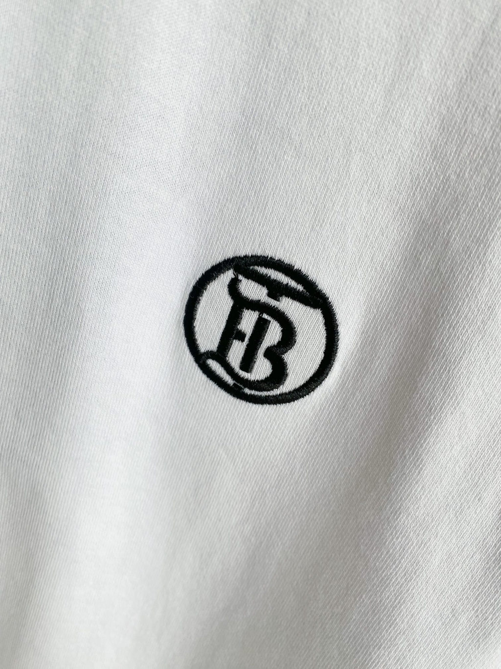 Close-up of small black circular logo embroidery on white T-shirt fabric.