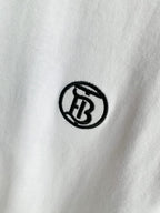 Close-up of small black circular logo embroidery on white T-shirt fabric.