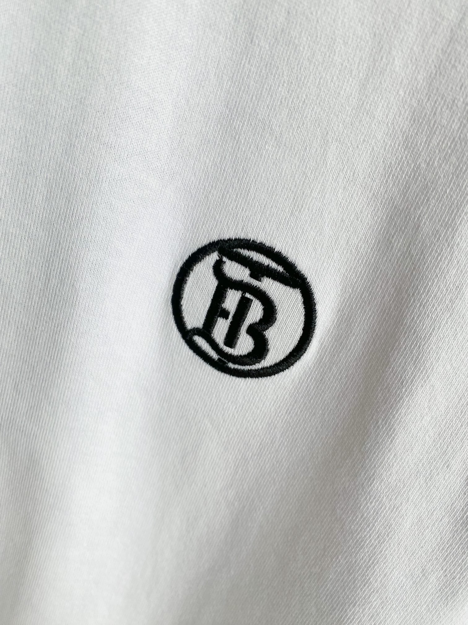Close-up of small black circular logo embroidery on white T-shirt fabric.