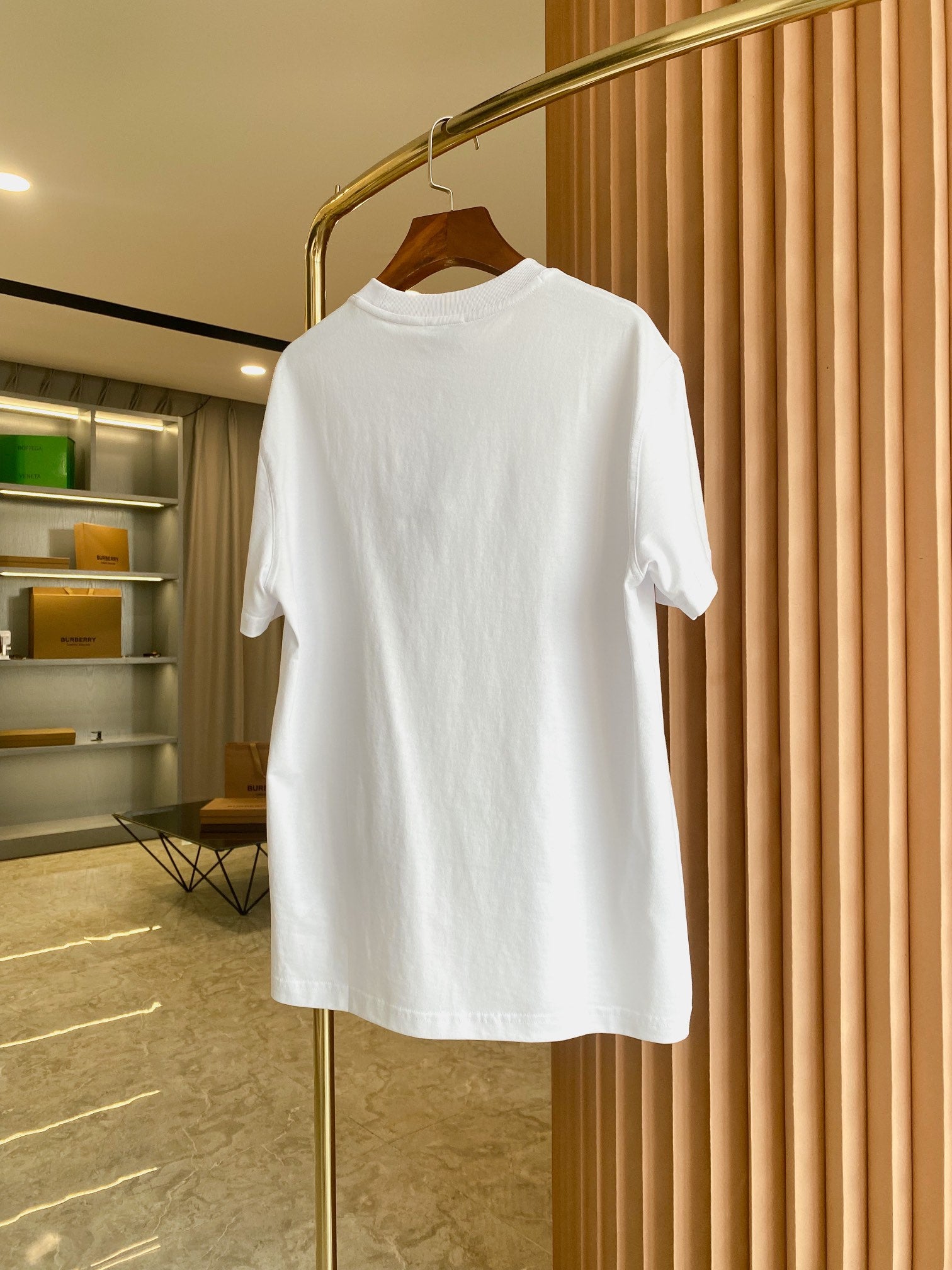 White short-sleeve crewneck T-shirt hanging on a gold hanger with chest logo.