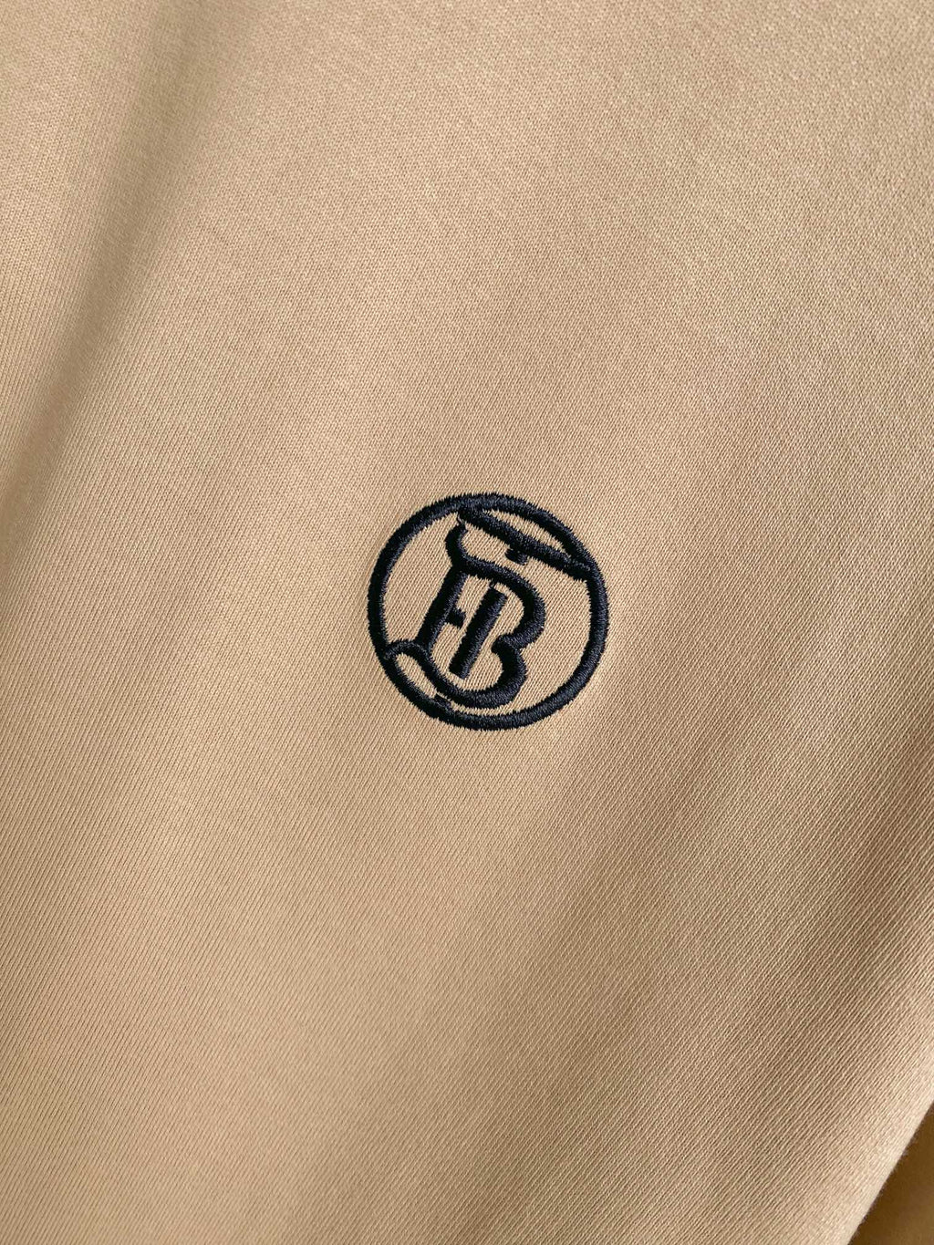Close-up of black circular logo on light beige short-sleeve T-shirt fabric