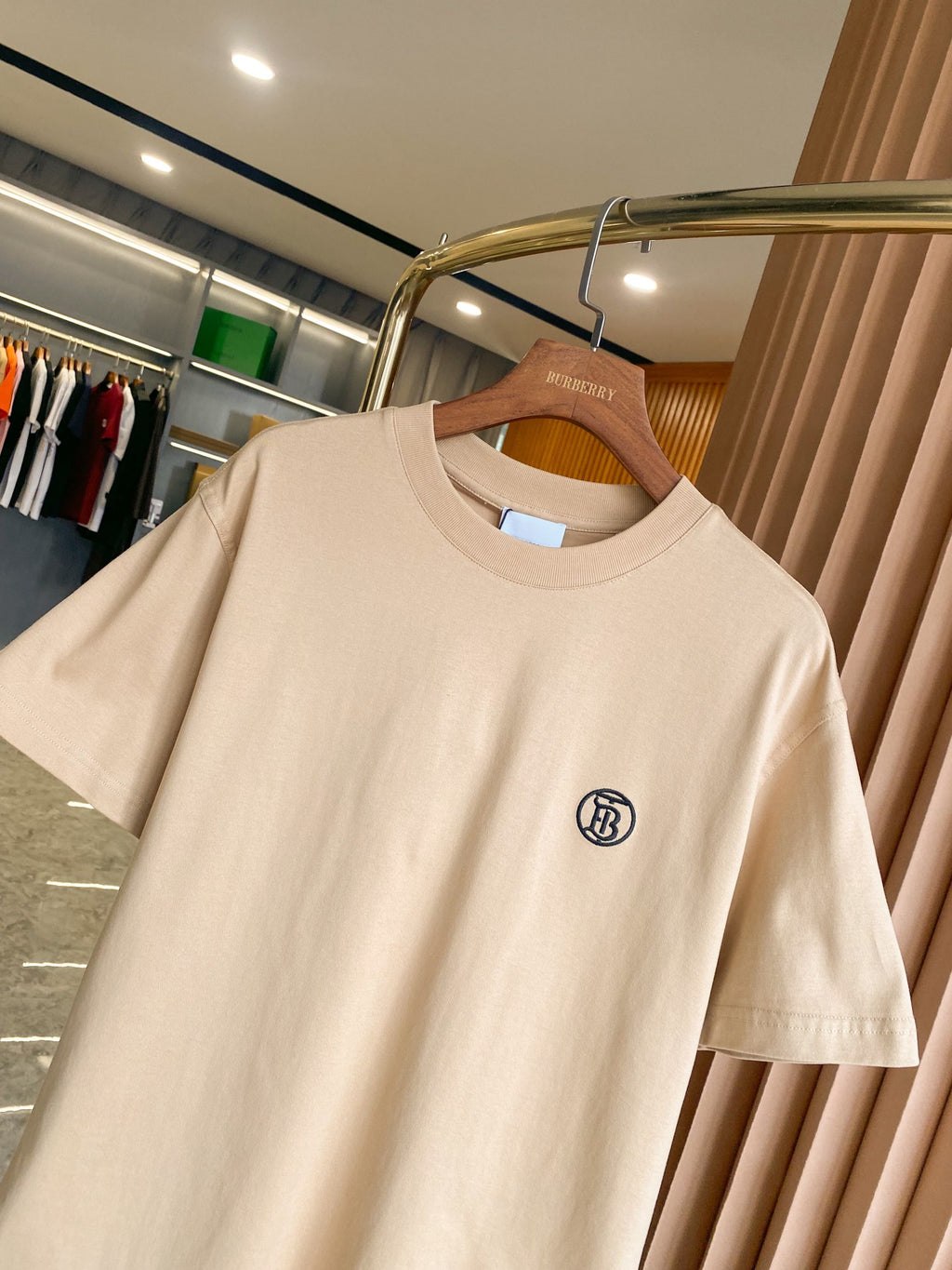 Light beige short-sleeve crewneck T-shirt with chest logo detail, on wooden hanger