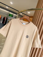 Light beige short-sleeve crewneck T-shirt with chest logo detail, on wooden hanger