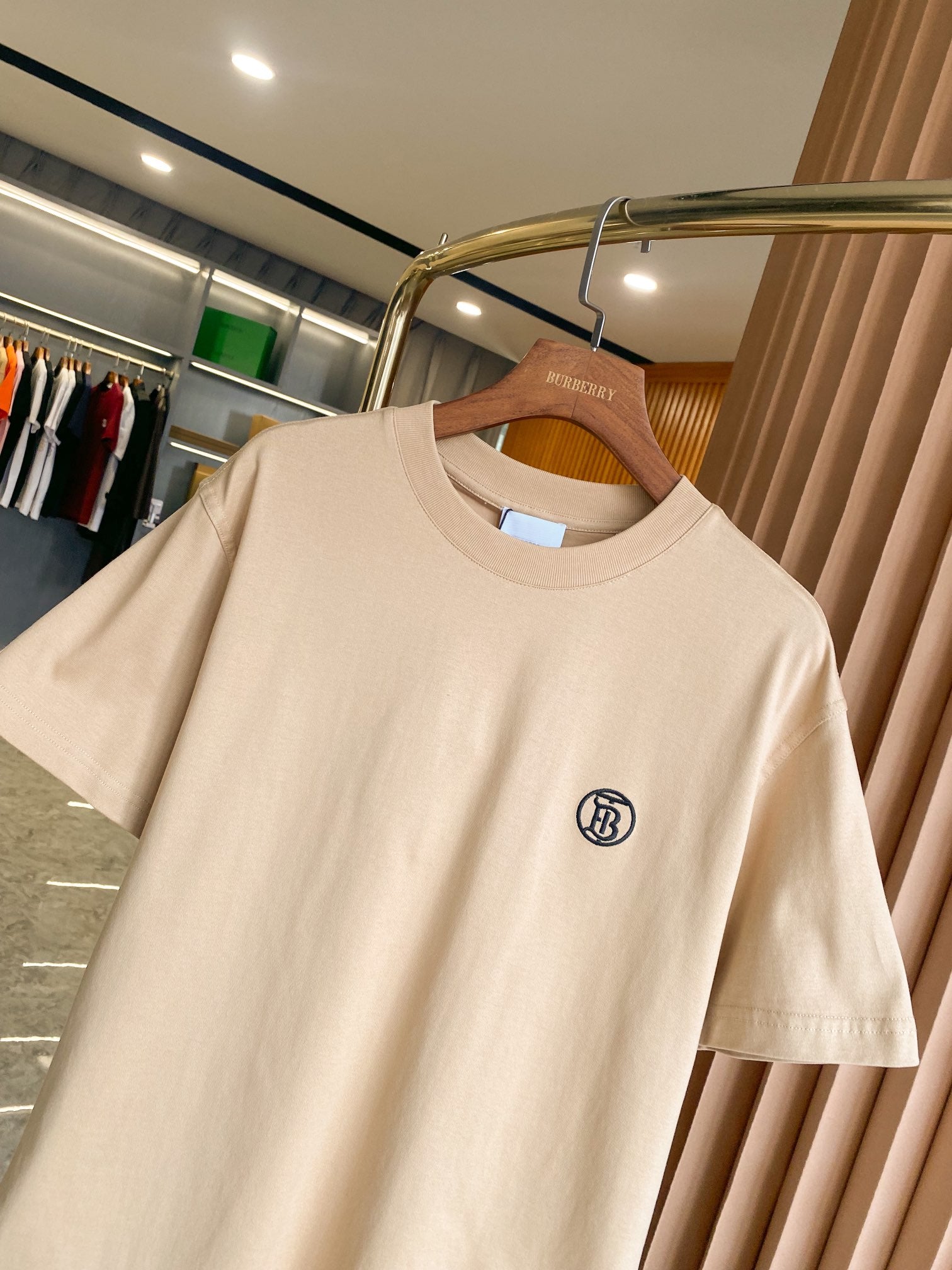 Light beige short-sleeve crewneck T-shirt with chest logo detail, on wooden hanger