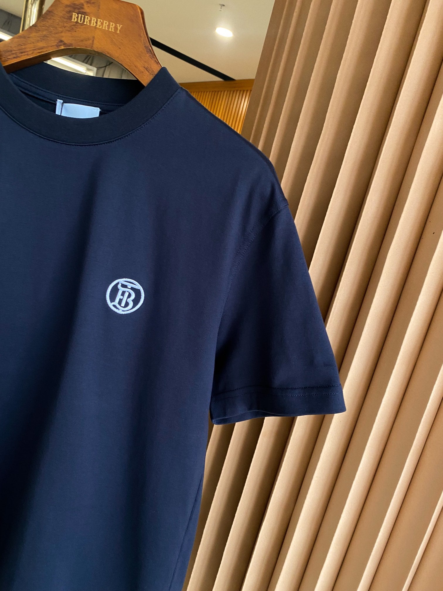 Navy crew-neck T-shirt with white circular emblem logo on left chest.