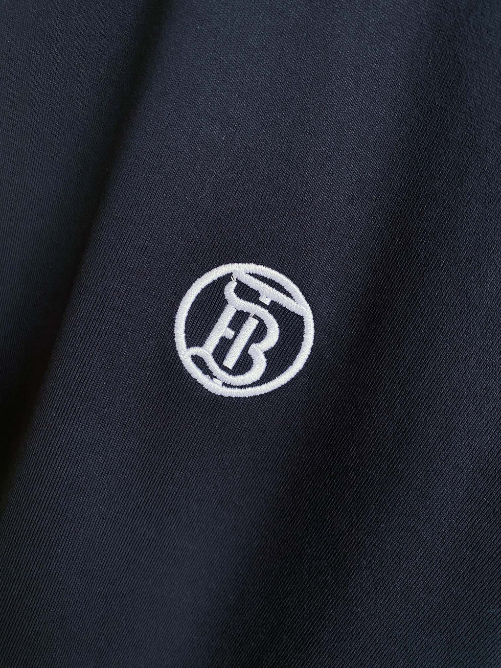 Navy T-shirt fabric close-up with white circular logo emblem.