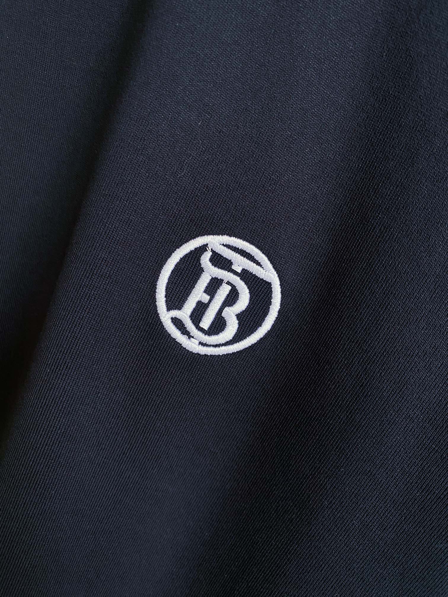 Navy T-shirt fabric close-up with white circular logo emblem.