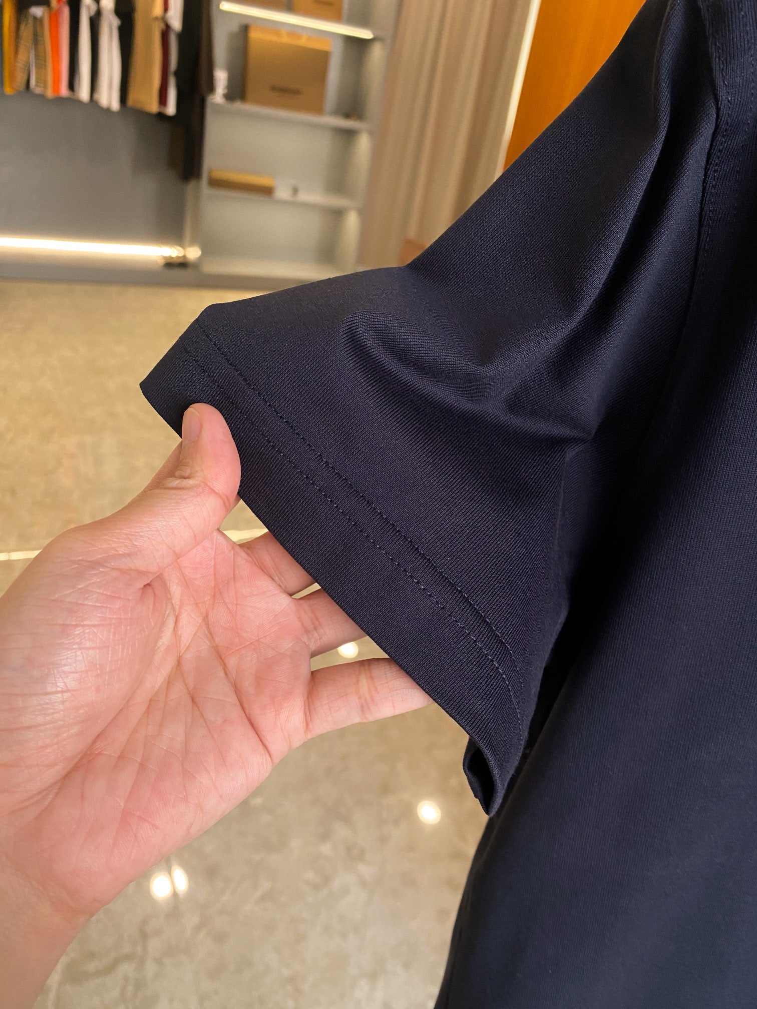Navy short-sleeve T-shirt cuff and side seam detail held by hand.