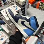 High-top Air Jordan 1 sneaker with navy, light blue, and white overlays and Swoosh