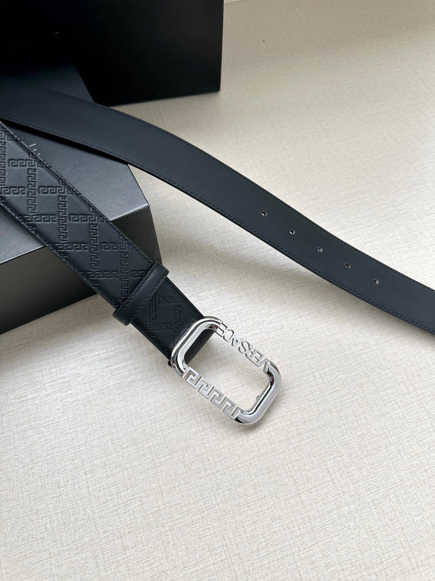 Versace belt with dark embossed strap and silver-tone rectangular buckle.