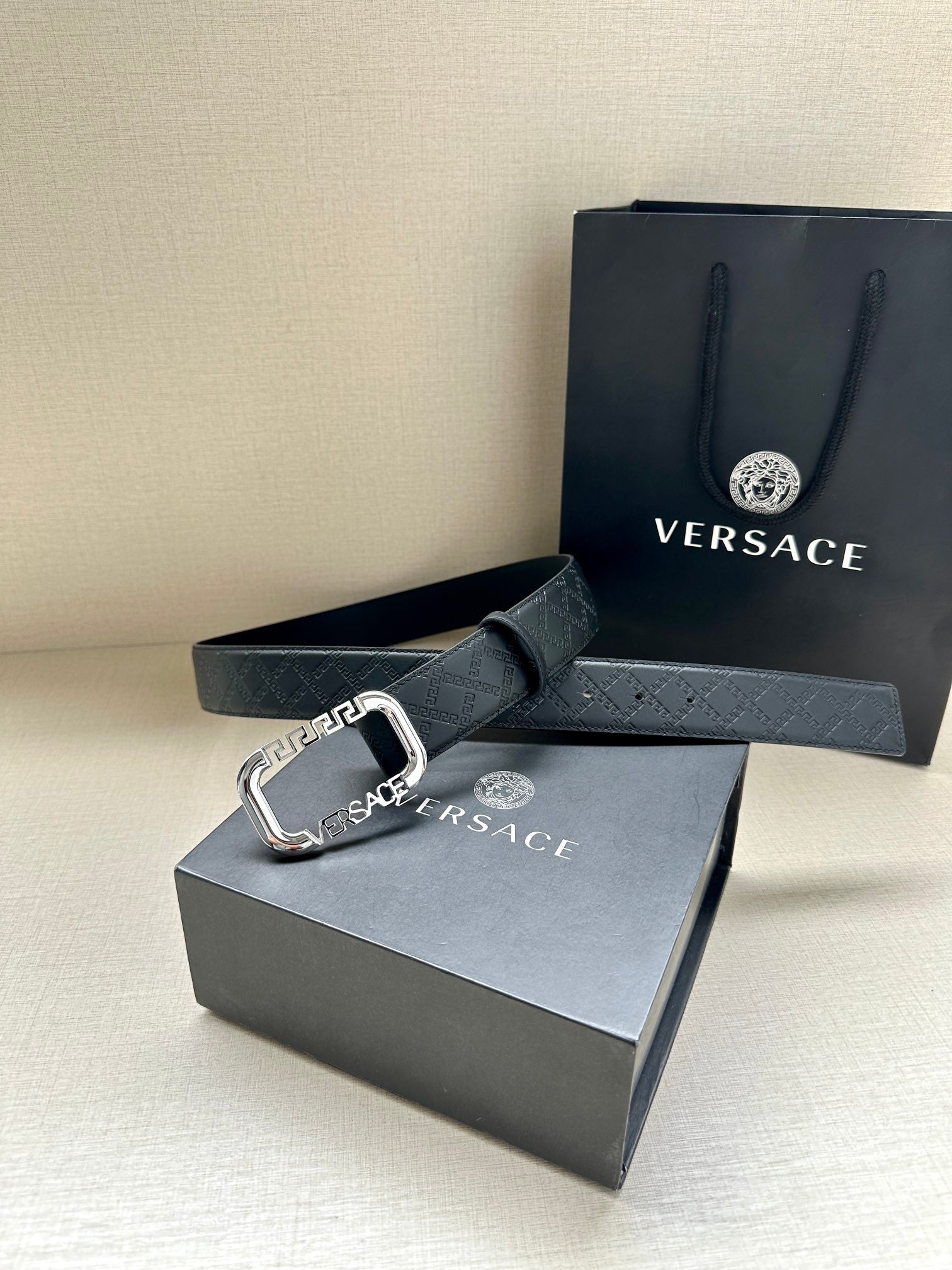 Versace belt with dark embossed texture and silver-tone buckle on strap end.