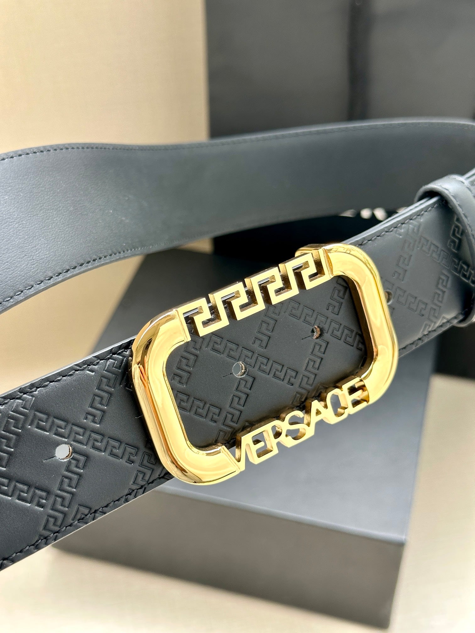 Versace belt with embossed logo print and gold-tone buckle on dark strap.