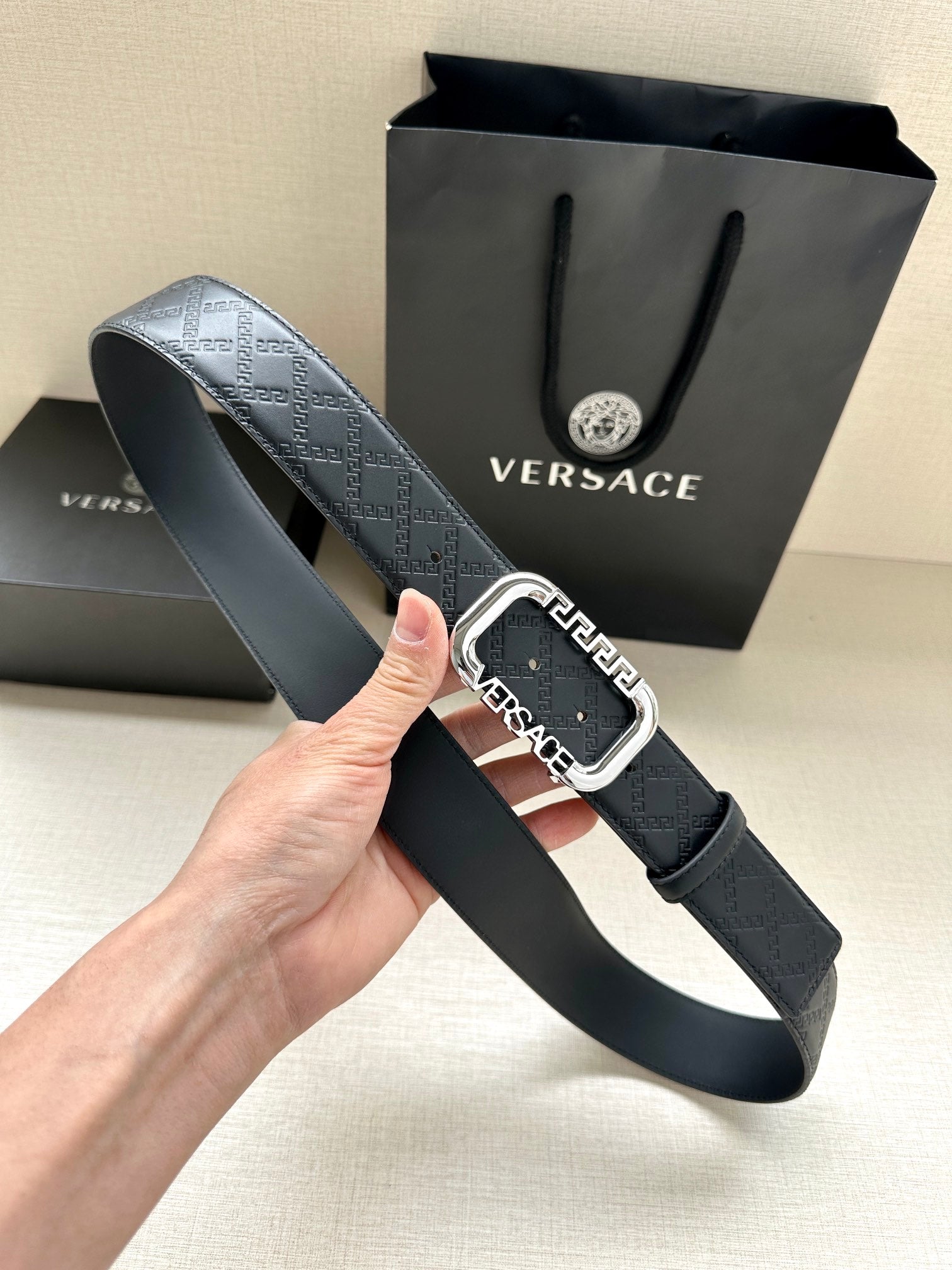 Versace belt with dark embossed strap and silver-tone buckle close-up.