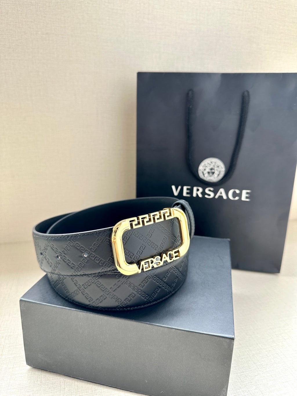 Versace belt in dark with embossed logo pattern and gold-tone square buckle.