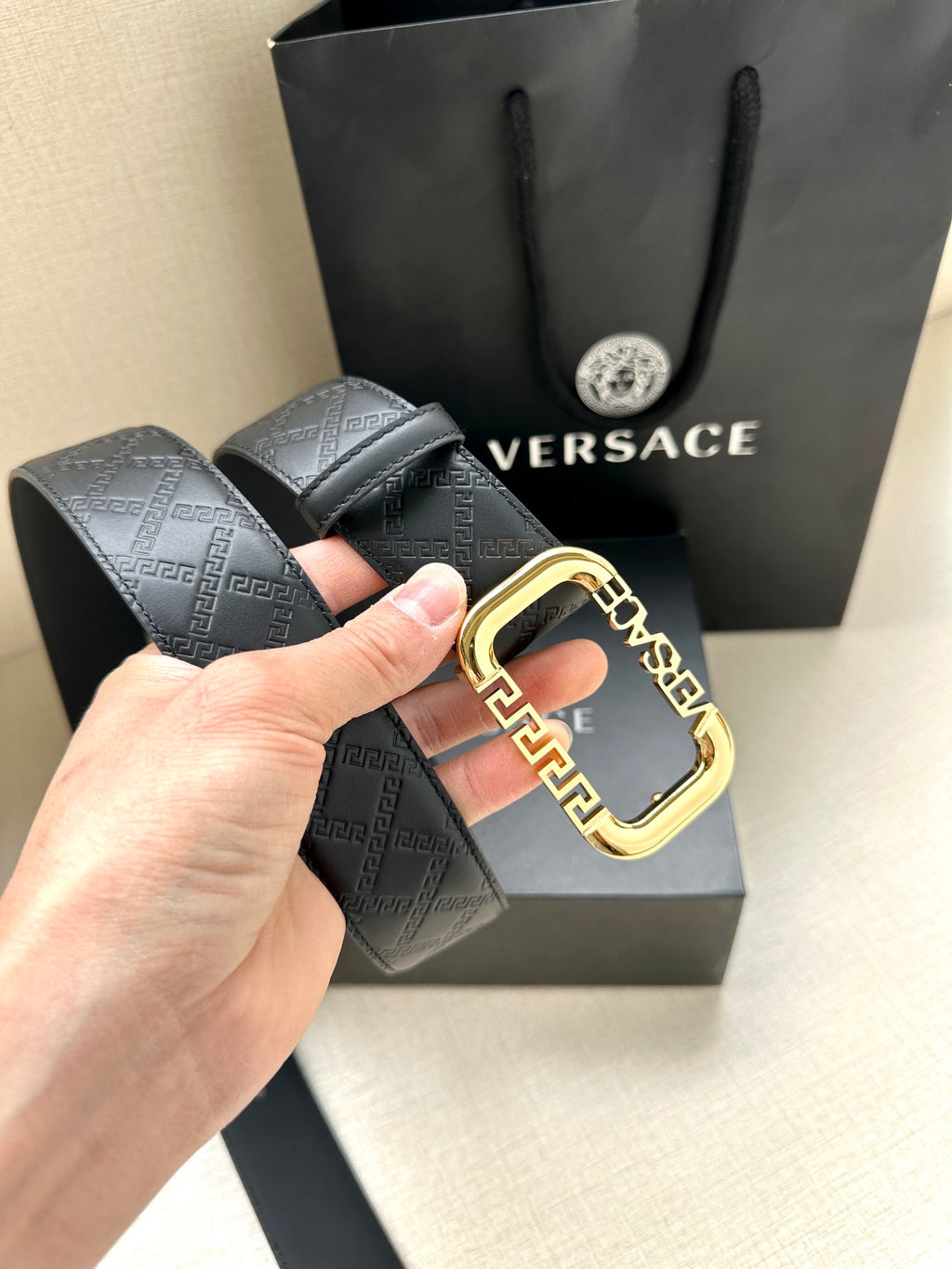 Versace belt with dark embossed pattern and gold-tone square buckle detail.