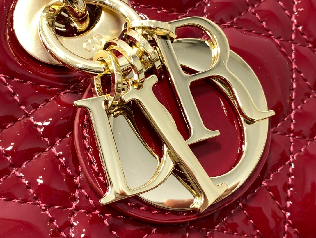 Dior handbag logo charm close-up on glossy deep red quilted leather.