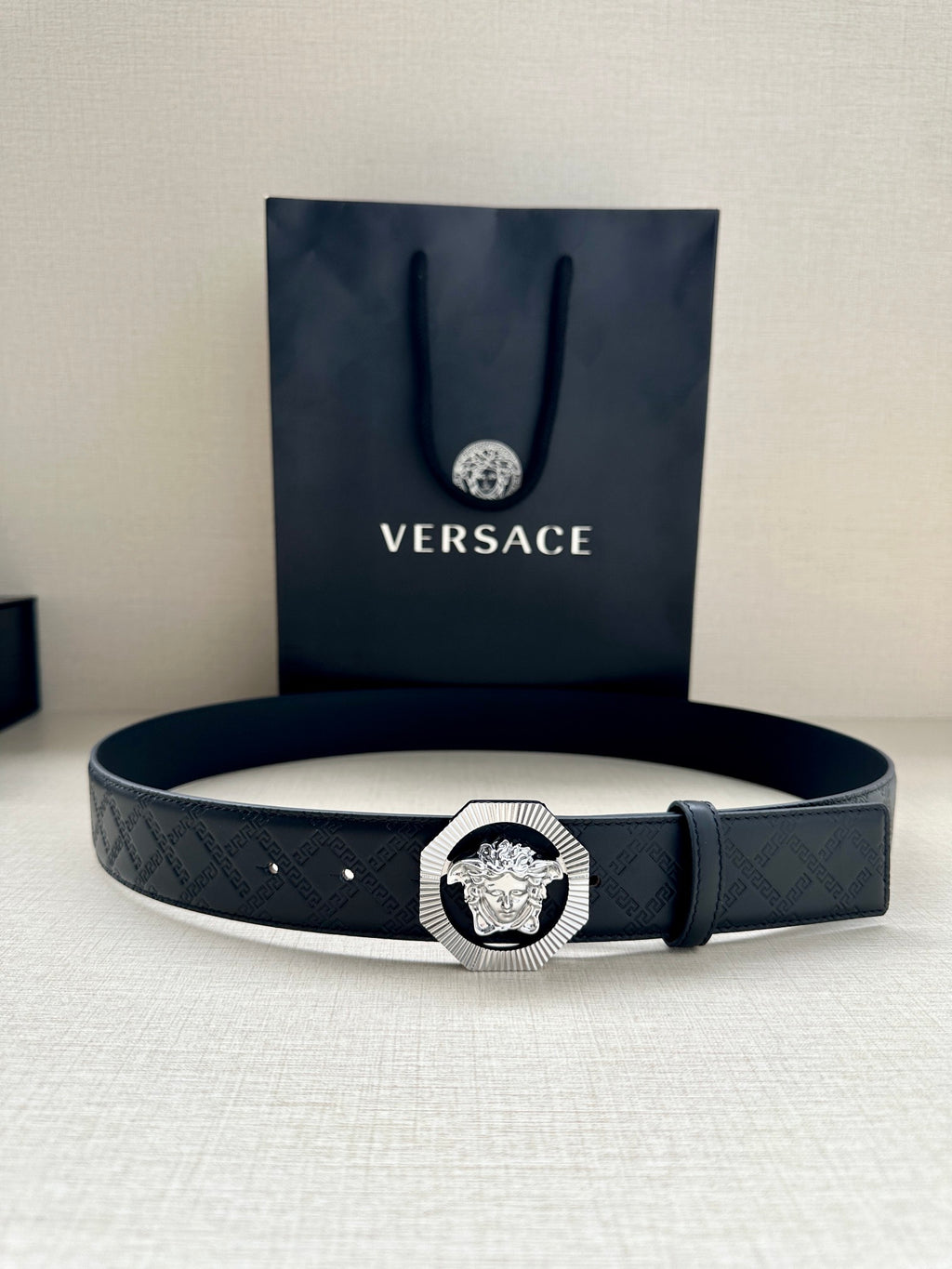 Versace belt with dark embossed strap and lion medallion buckle, laid flat