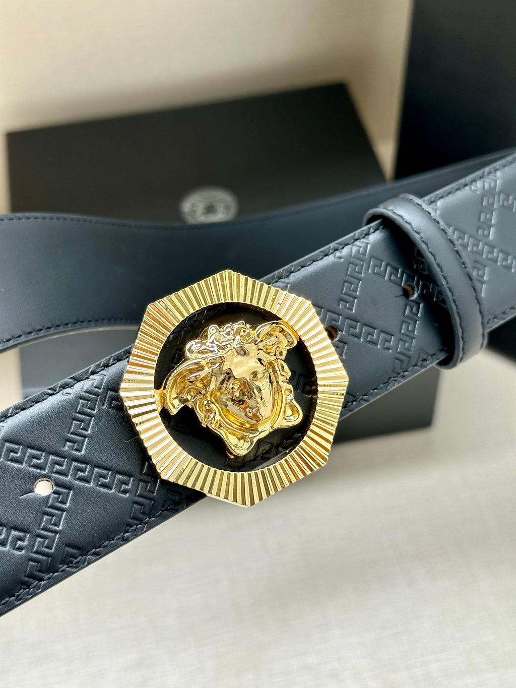 Versace belt close-up showing embossed pattern strap and lion medallion buckle
