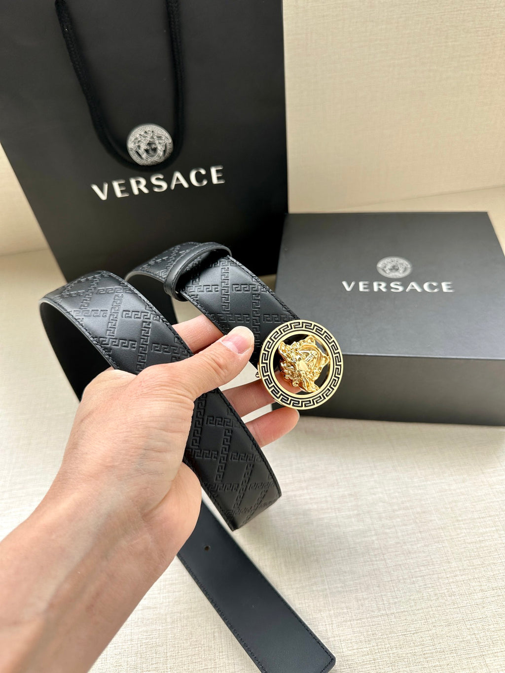 Dark leather monogram belt with gold Medusa buckle held for close-up