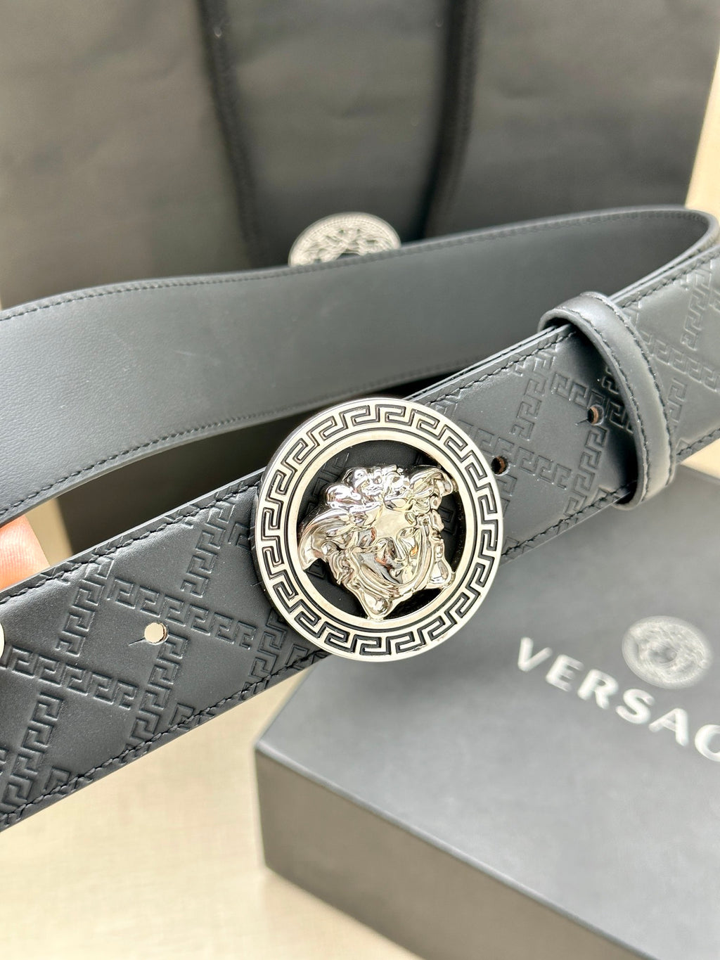 Dark leather belt with monogram texture and close-up gold Medusa buckle