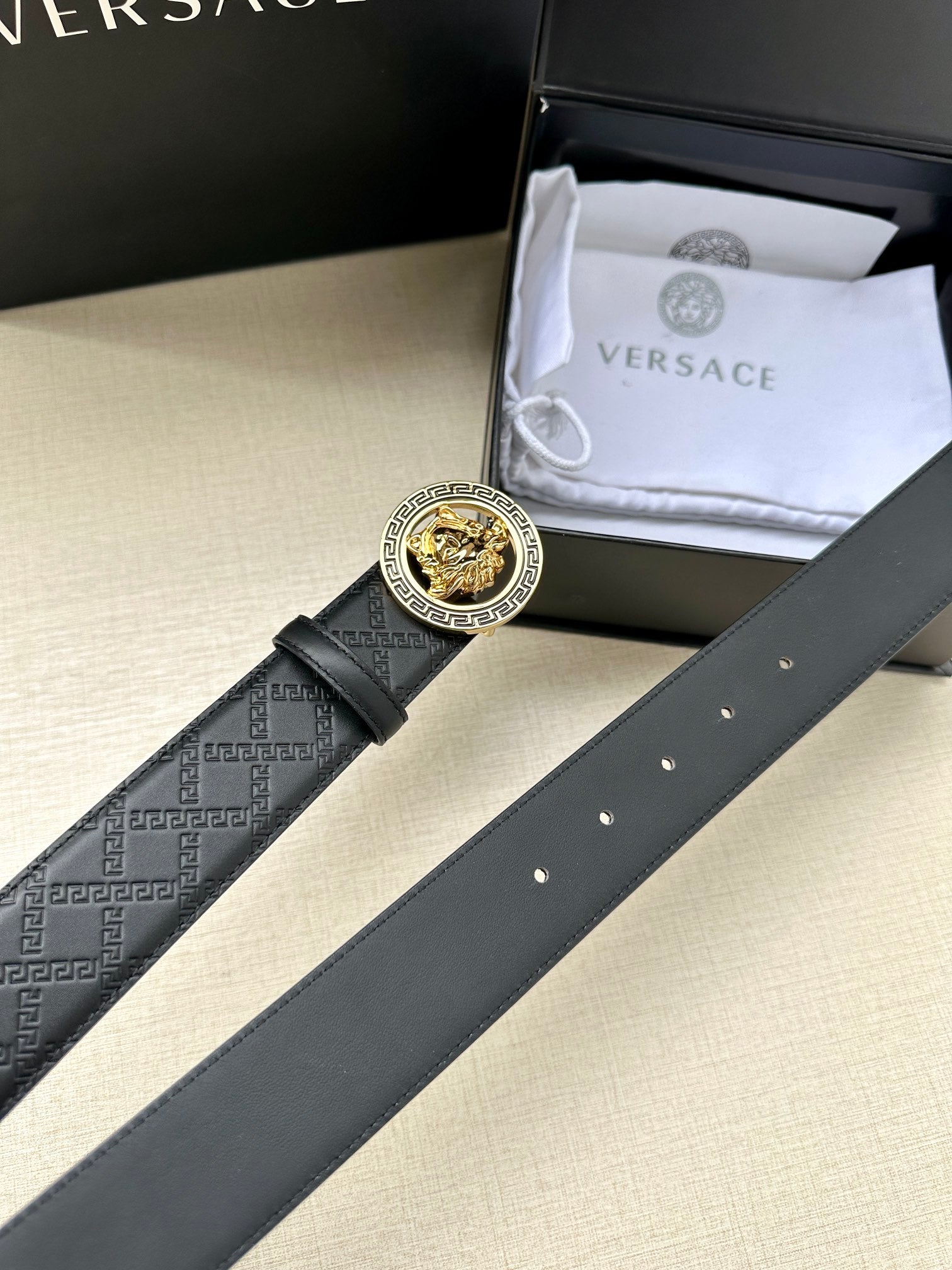 Dark leather belt with gold Medusa buckle and embossed monogram strap