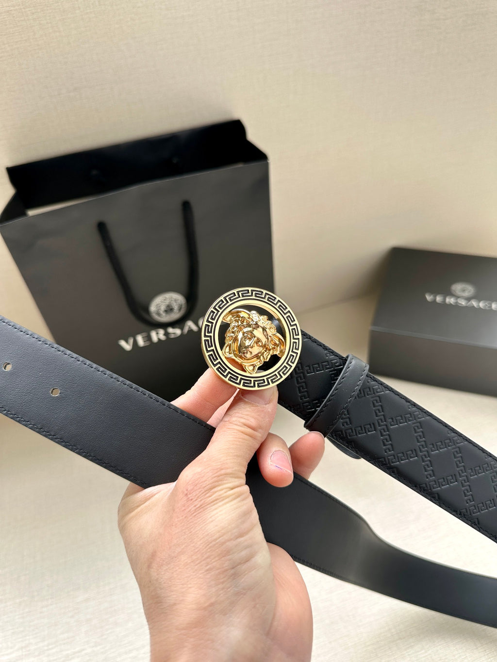 Dark leather belt with round gold Medusa buckle shown in hand