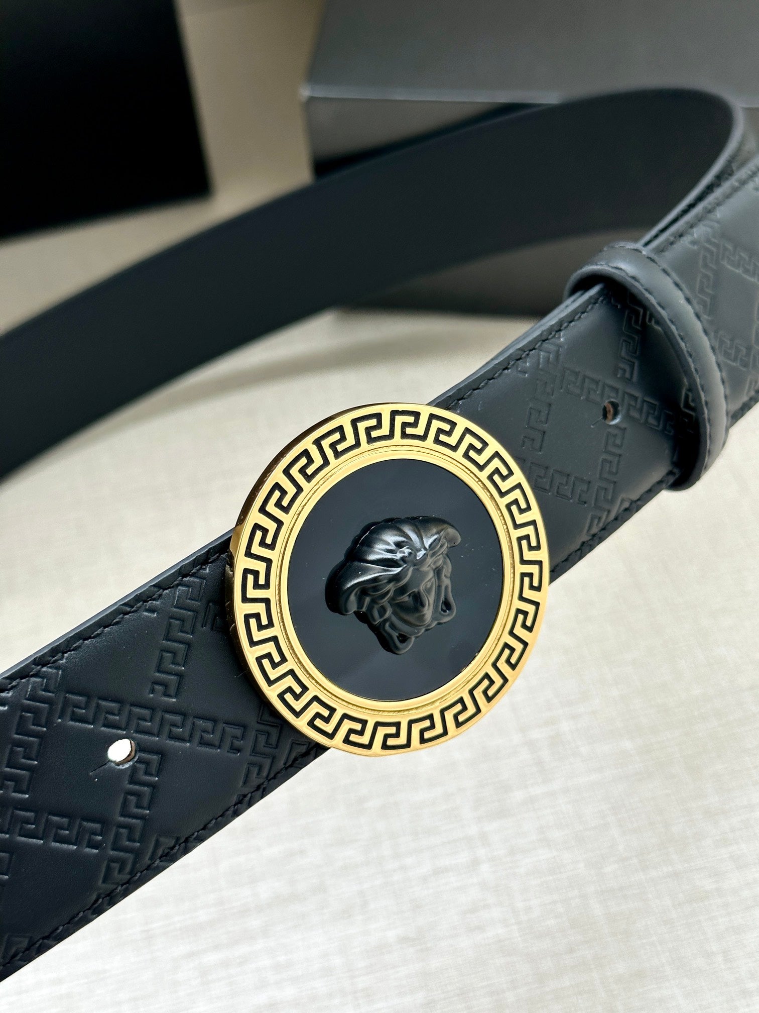 Dark navy belt buckle close-up with gold Greek key frame and lion emblem