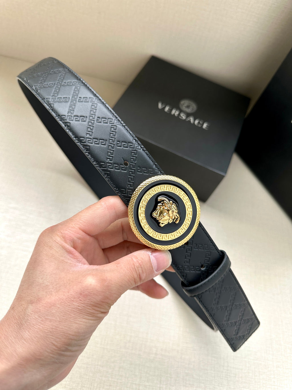 Versace belt in dark leather with embossed monogram and round gold-and-black medallion buckle