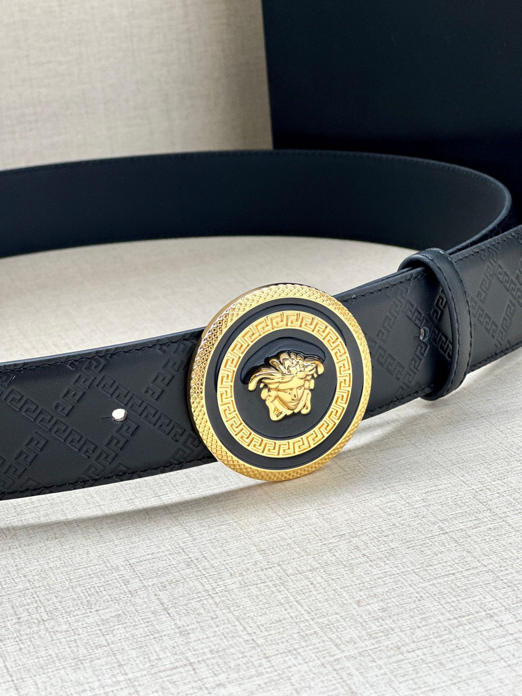 Versace belt close-up: dark embossed strap with round medallion buckle and gold trim