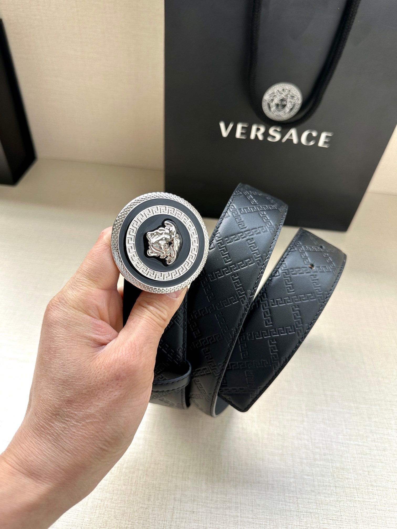 Versace belt detail view: round medallion buckle and dark embossed monogram strap