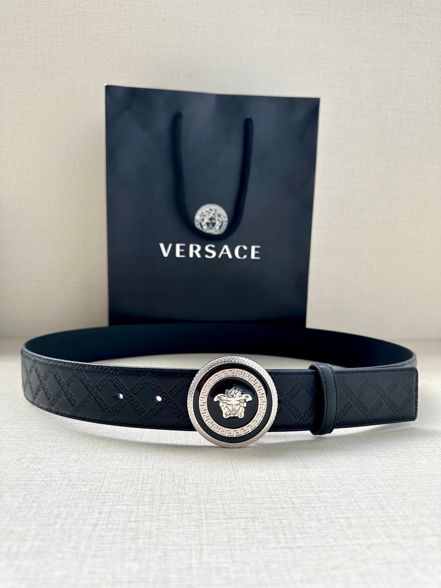 Versace belt lying flat: dark embossed strap with round medallion buckle
