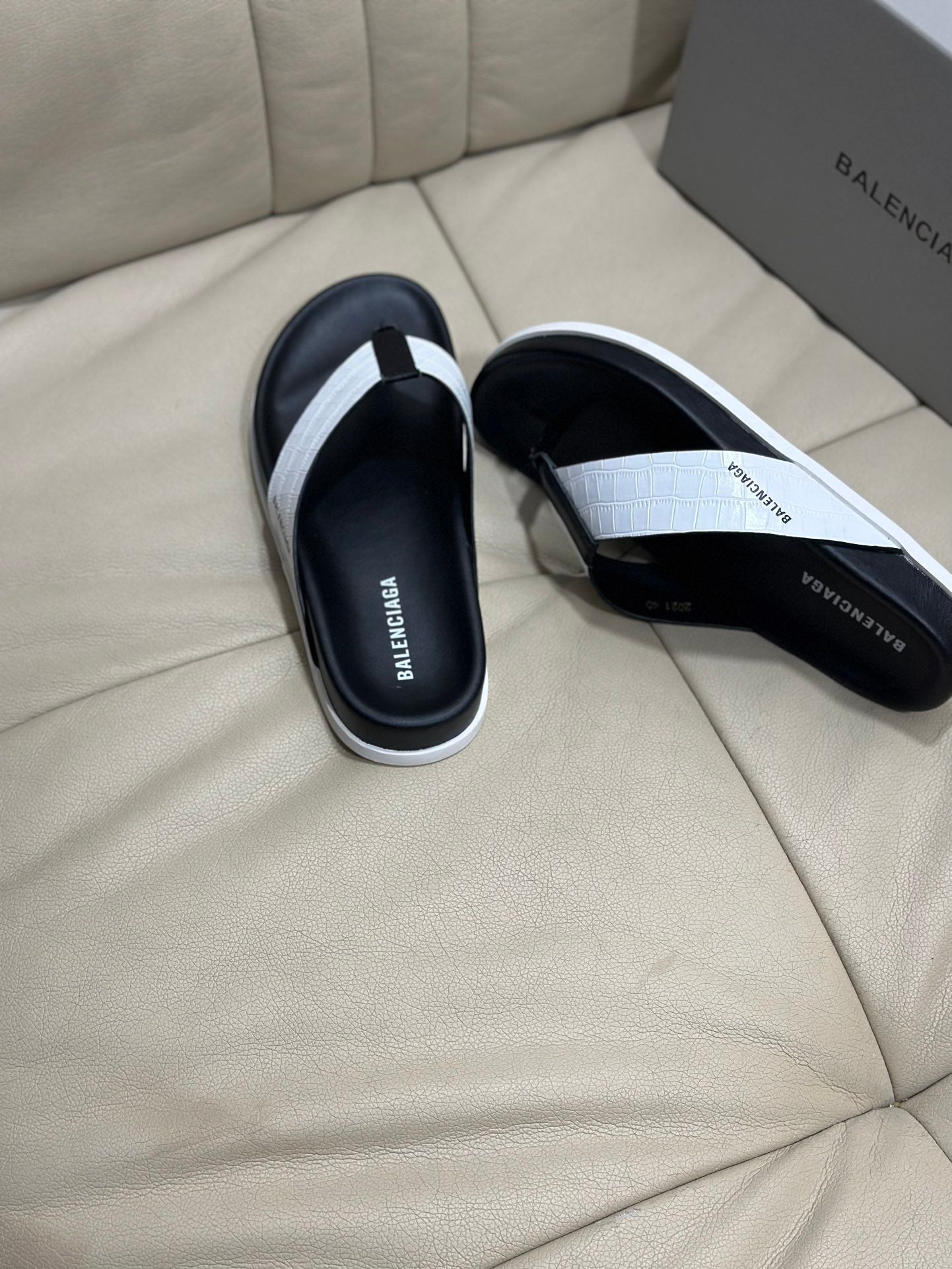 Two-tone flip-flop sandals with white strap and black footbed, laid on couch