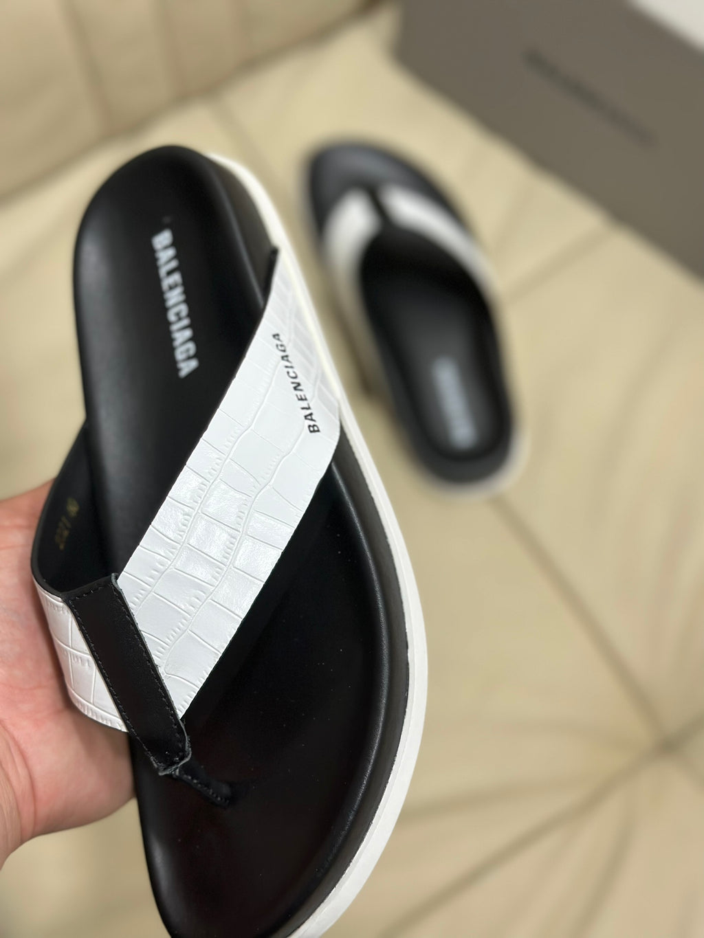 Handheld close-up of black and white sandals with croc-textured strap panel
