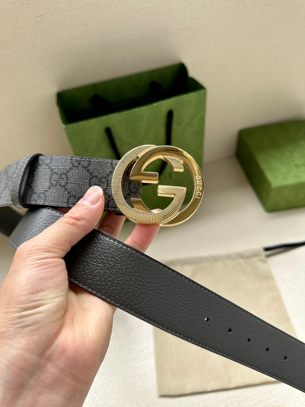Gucci belt buckle close-up on dark gray GG canvas strap held in hand