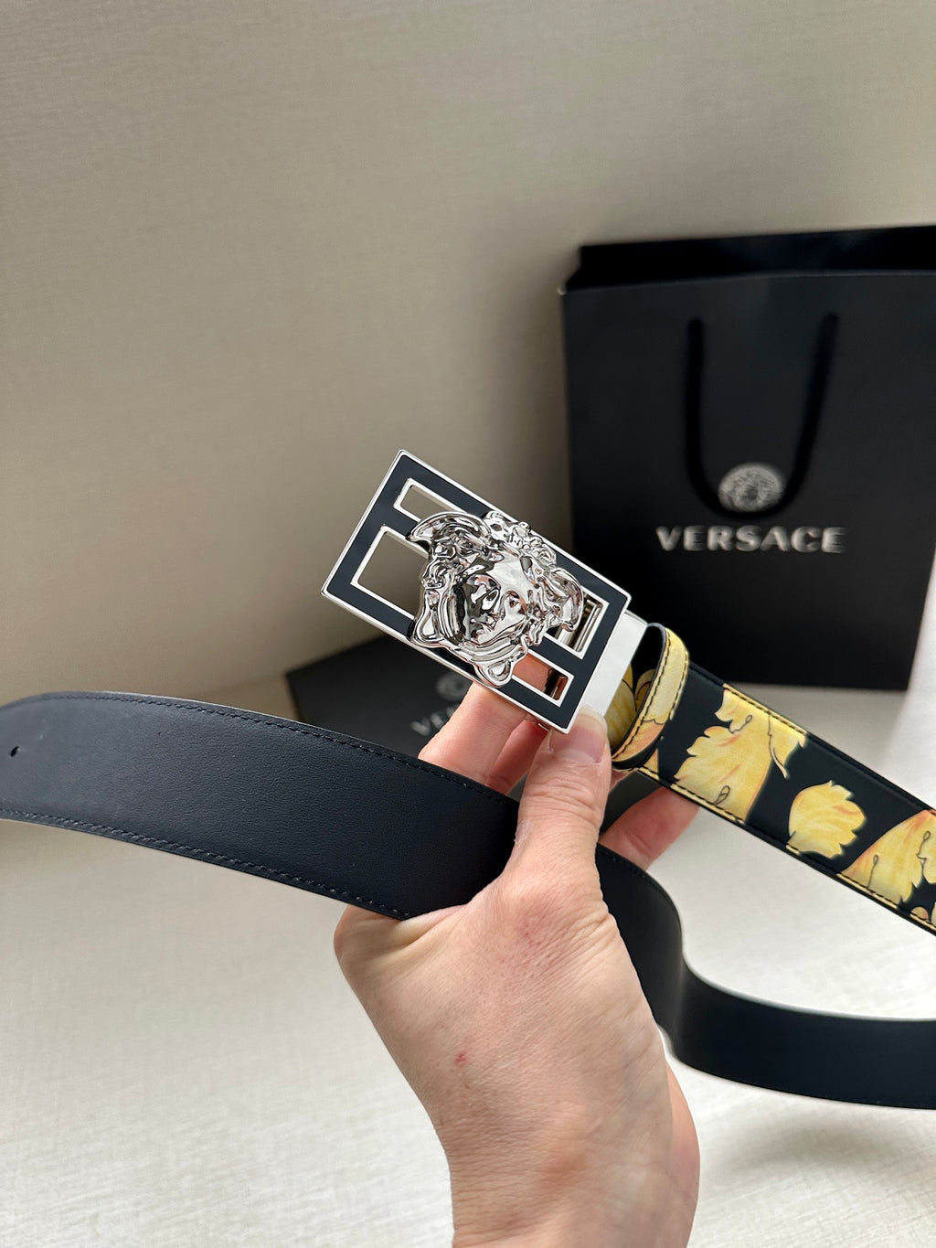 Versace belt hand-held close-up: navy strap with gold flowers and silver-tone Medusa buckle.