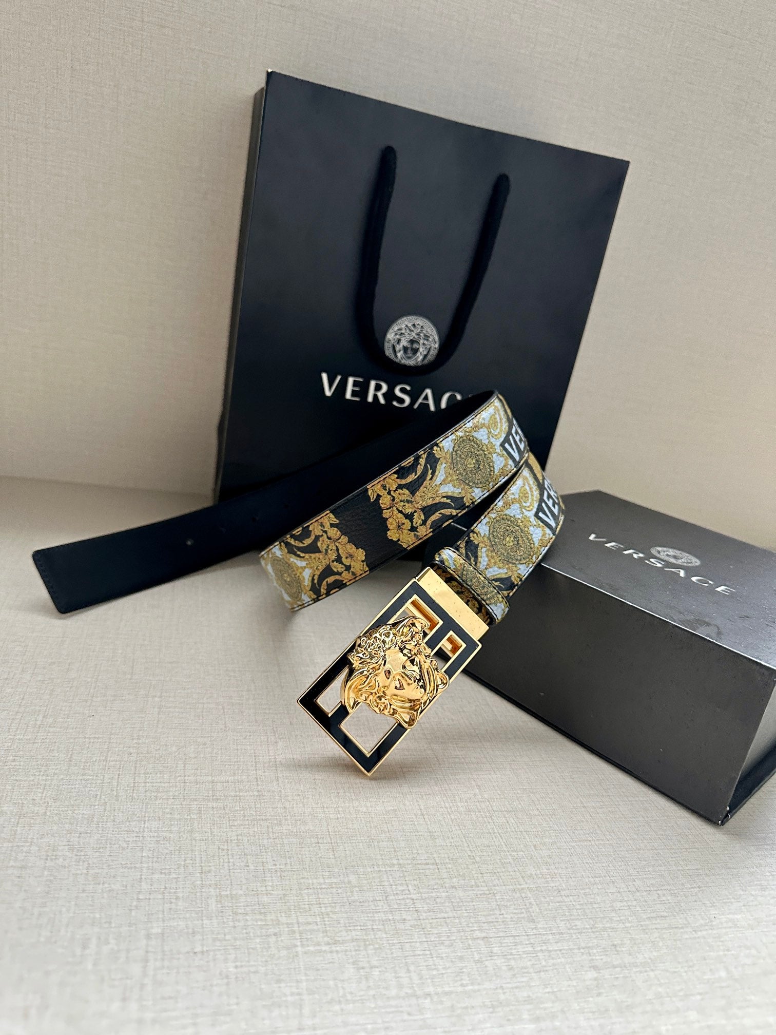 Versace belt with gold-blue patterned strap and gold square buckle, laid diagonally