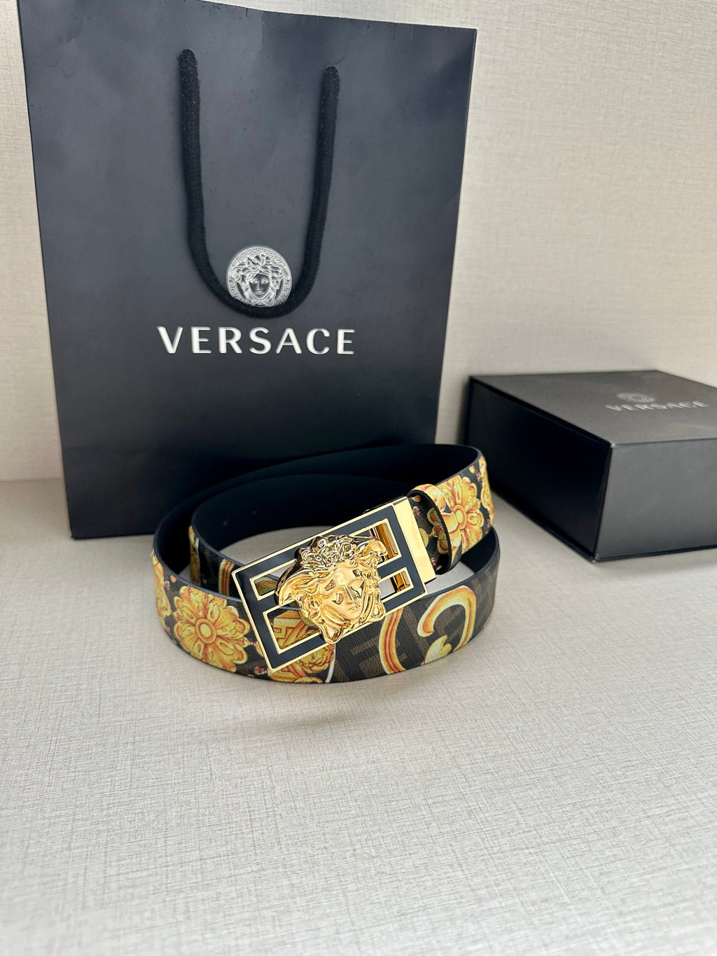 Designer belt with navy patterned strap and gold buckle resting on surface
