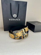 Designer belt with navy patterned strap and gold buckle resting on surface