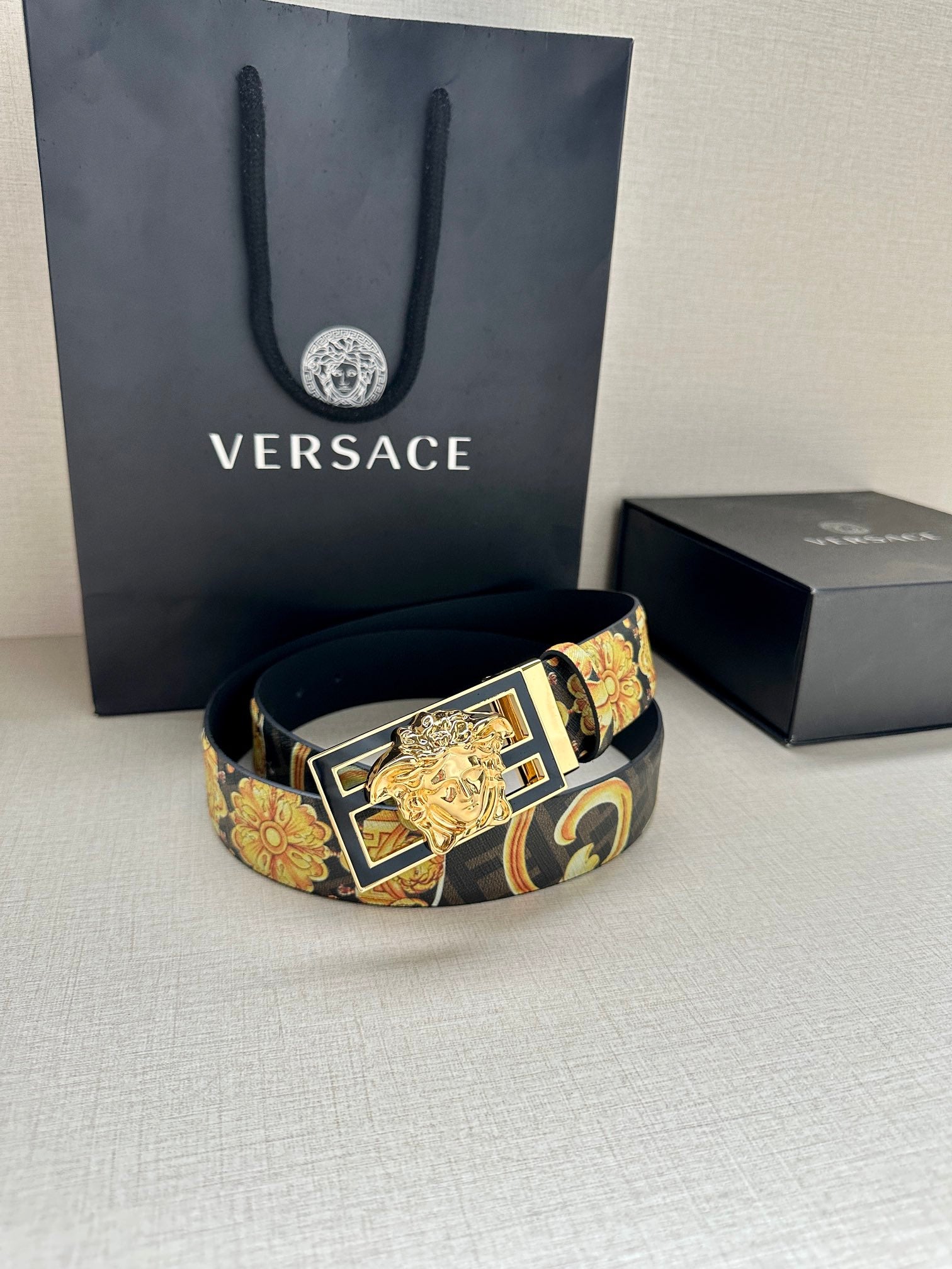 Designer belt with navy patterned strap and gold buckle resting on surface