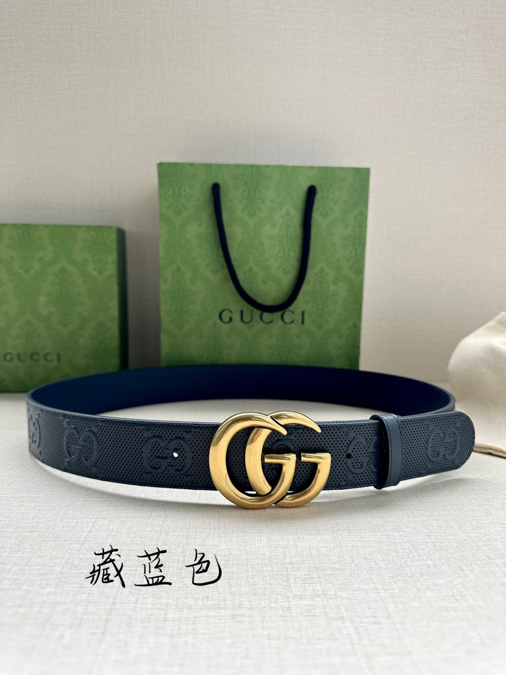 Gucci belt flat lay, dark blue strap with embossed GG pattern and gold-tone buckle