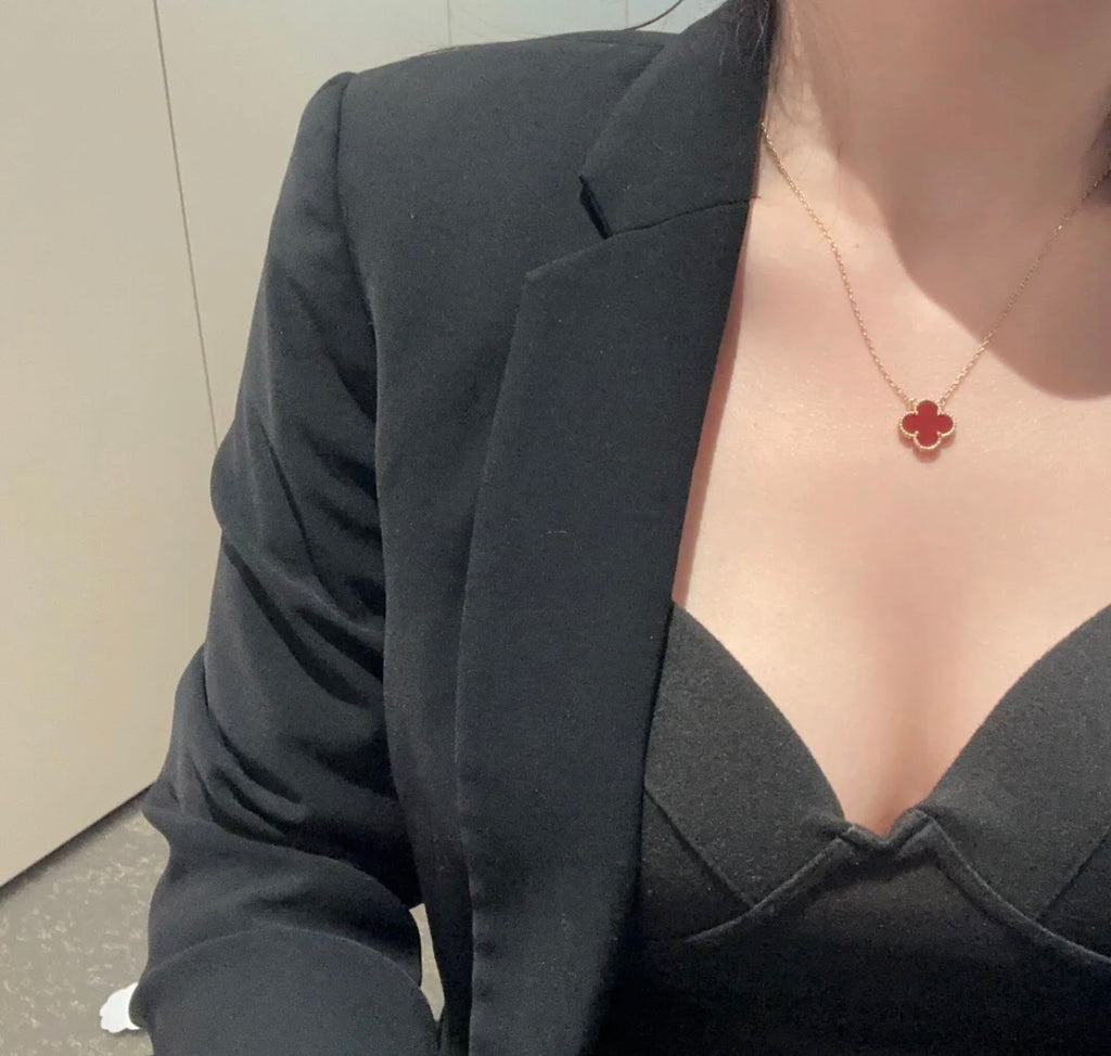 Gold clover pendant necklace worn at the neckline with dark top