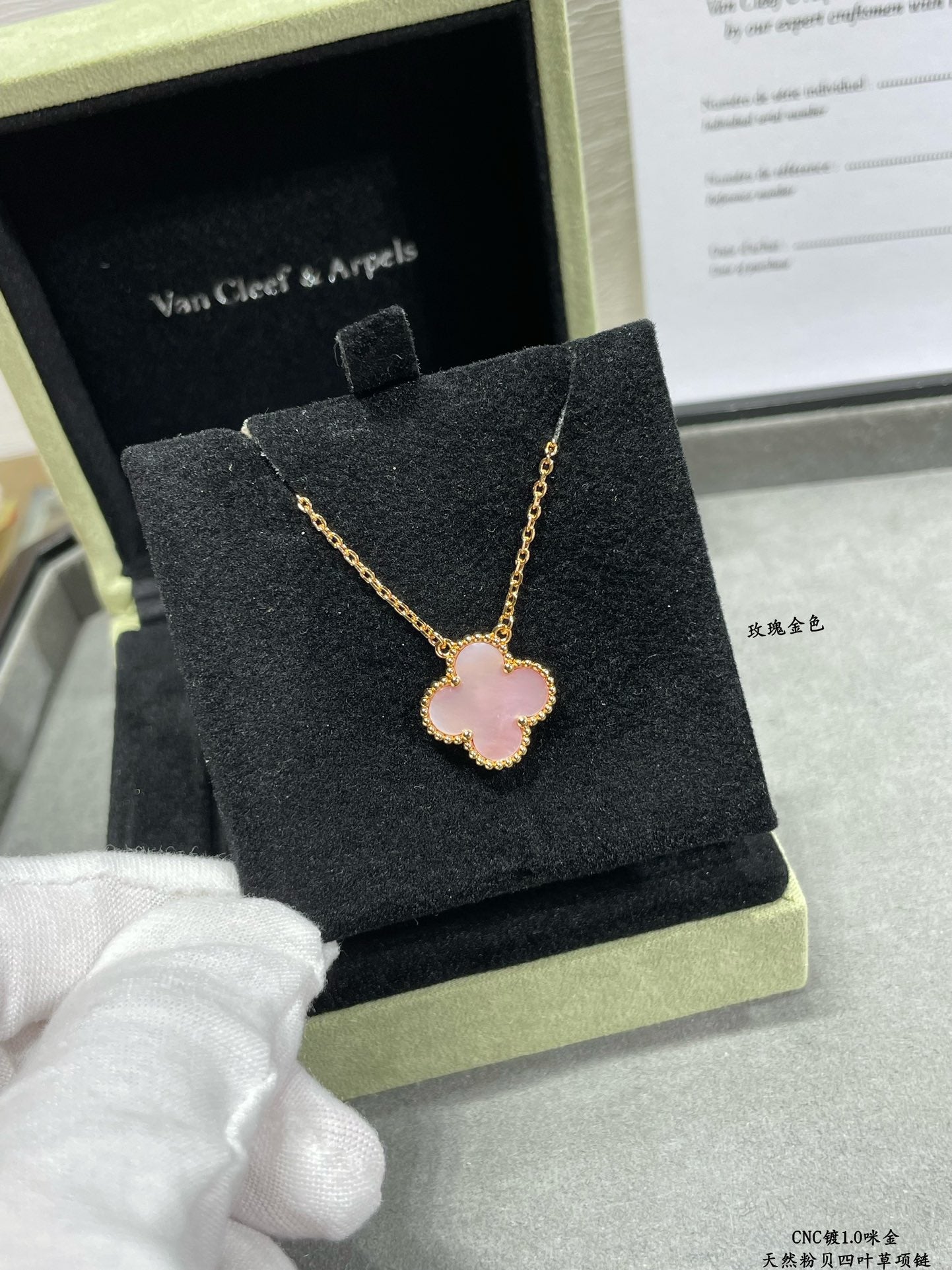 Gold-tone necklace with pink clover pendant on a black jewelry box cushion.