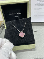 Silver-tone necklace with pink clover pendant on a black jewelry box cushion.