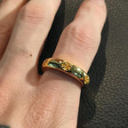 Gold-colored ring on finger with dark inlay and small floral accents along the band.